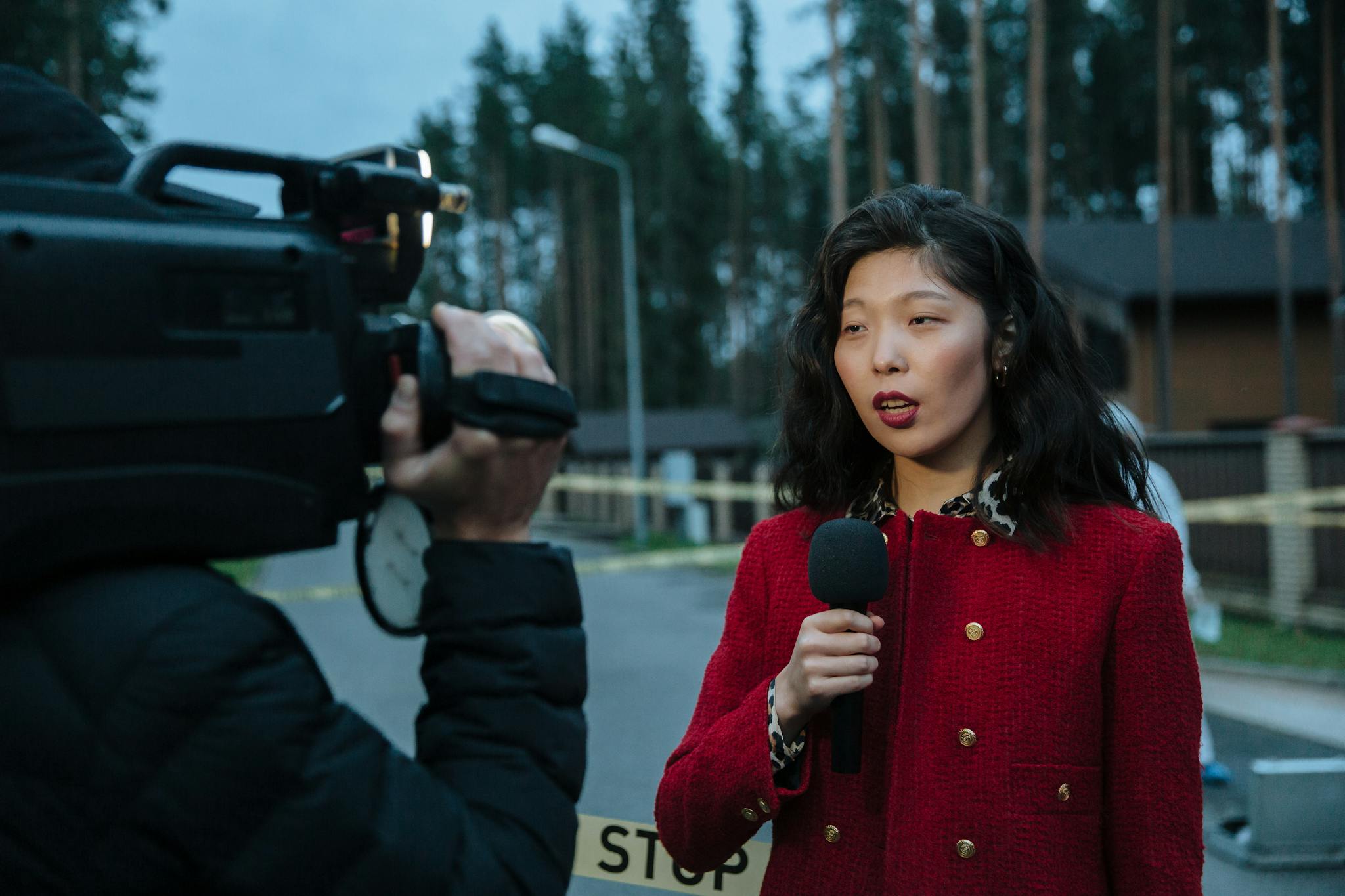Asian female journalist reporting live from a suburban crime scene with camera and microphone.
